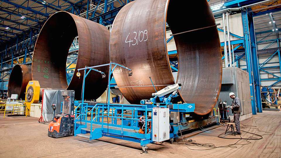 Ein Mitarbeiter von Steelwind Nordenham arbeitet in einer Produktionshalle an einem Teilstück eines Stahlfundaments für Windkraftanlagen auf See.