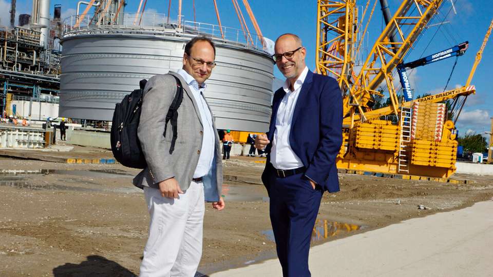 Raffinerie-Chef Lars Bergmann (rechts) hat sich mit DVZ-Autor Kai Eckert getroffen. Im Hintergrund wird der neue Tankbehälter auf dem Fundamentsockel abgesetzt.