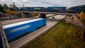 Ein Lkw auf der Autobahn A100 bei Potsdam in Brandenburg, gekreuzt von einem Güterzug auf einer Eisenbahnbrücke.